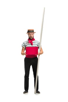 Caucasian funny bearded man in traditional gondolier costume and hat with paddle standing with mobile phone at studio isolated on white background. young man. Human emotions, facial expression concept