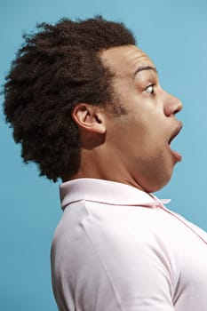Wow. Attractive male half-length front portrait on blue studio backgroud. Young emotional surprised bearded man standing with open mouth. Human emotions, facial expression concept. Trendy colors. Profile