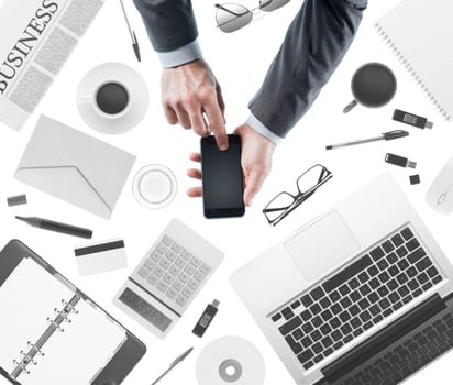 Businessman using a touch screen smartphone, desktop with laptop on background, top view