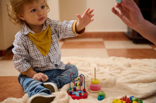 A small child explores colorful educational toys on a blanket, engaging in a happy and focused activity, while a guiding hand supports learning through play.