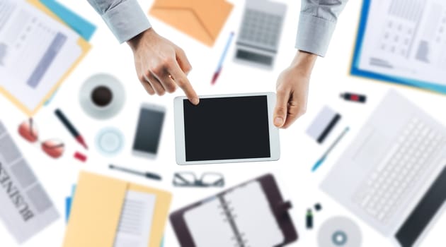 Businessman using a digital touch screen tablet, hands close up top view, desktop on background