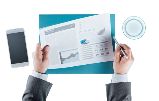 Businessman checking a financial report and holding a pen, hands close up, top view