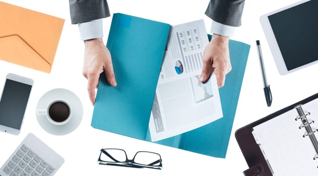 Businessman working at office desk and holding financial reports, hands close up, top view