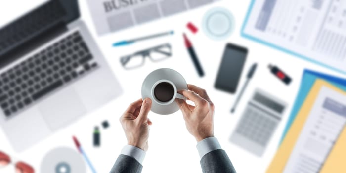 Businessman holding an espresso and having a coffee break, desktop on background, top view