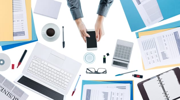 Business woman working at office desk and using a smart phone, unrecognizable person, top view