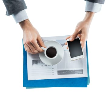 Businessman having a coffee break and using a smart phone, hands close up, top view