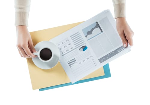 Business woman having a coffee at office desk while reading a financial report, hands close up