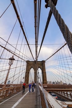 Brooklyn Bridge, New York, United States - June 08, 2015: People walk and while other tourists observe, from the bridge, the Manhattan skyline.