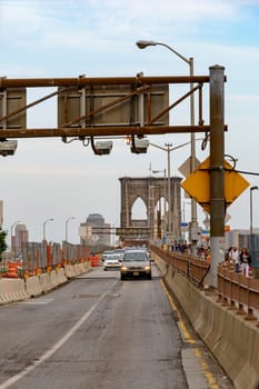 Brooklyn Bridge, New York, United States - June 08, 2015: People walk and while other tourists observe, from the bridge, the Manhattan skyline.