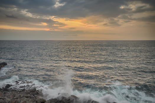Landscape of an ocean sunset with waves crashing on the rocks below, Kona, Hawaii.