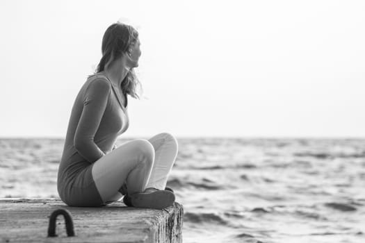 A young girl sits on a pier and looks out into the distance at sea