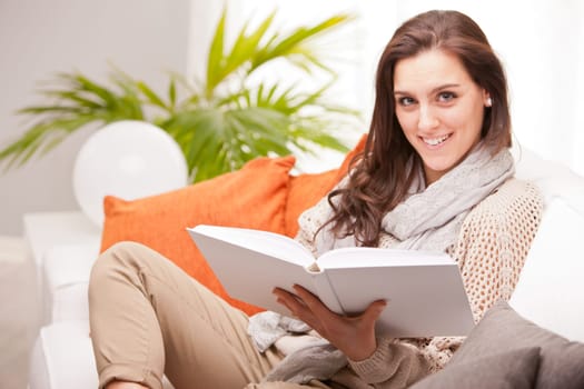 beautiful fascinating woman reading a book in her living room on a white sofa
