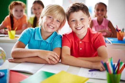 Two cheerful schoolboys looking at camera in classroom