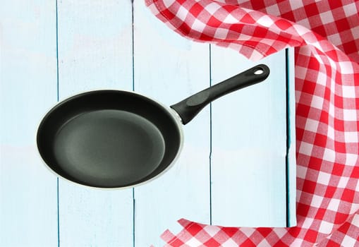 Empty pan and a red white checkered tablecloth on a wooden bright tabletop. concept food.