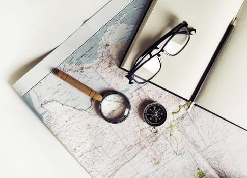 Stationery, travel accessories and vacation items. Vintage toned image. Flat lay. Top view. Map, notebook, magnifier, compass glasses and pencil