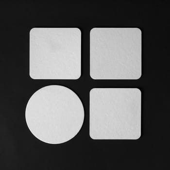 Four blank beer coasters on black paper background. Top view. Flat lay.