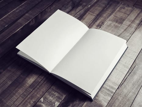 Photo of opened book with blank pages on wooden background. Vintage toned image.