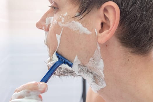 The guy shaves his left cheek, close-up