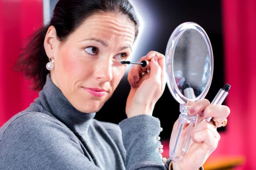 young dark haired woman looking in mirror and applying make up