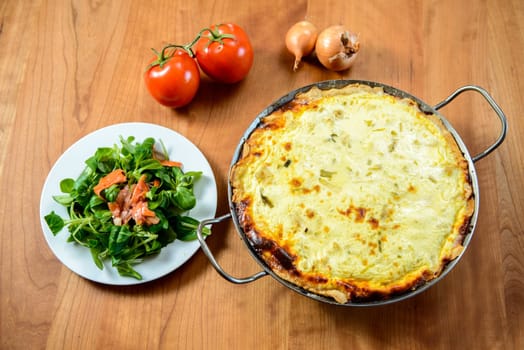 baked quiche with field salad on wooden table