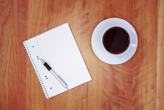 notepad with pen and a cup of tea on wooden table from above