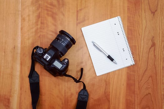 camera, notepad with pen and coffee on wooden table from above