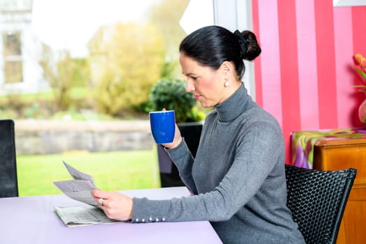 young dark haired woman at home with cup of coffeee reading newspaper
