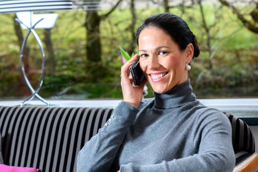 young dark haired woman at home sitting on sofa andcalling