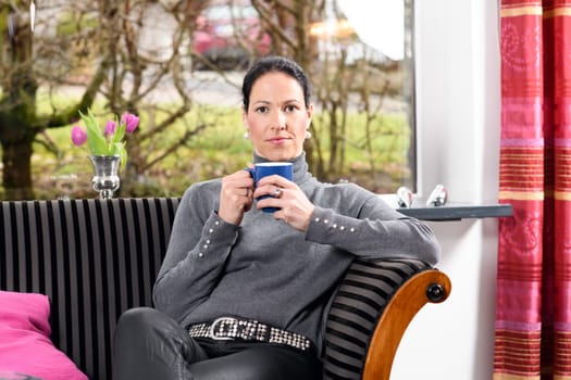 young dark haired woman at home with cup of coffeee relaxing