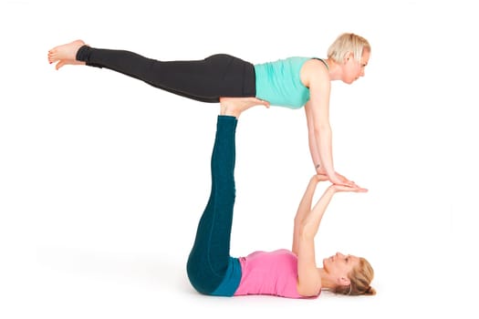 Full-body view of two young women lying on their backs lying on their backs with their legs outstretched upwards,whereupon the partner lies stretched out with the pelvis on the feet of the woman lying down against a white background with slight shadows.