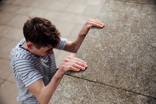Freerunner is suspended from the side of a building, gripping on with his hands.