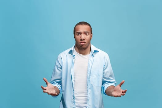 Why is that. Afro male half-length portrait isolated on trendy blue studio backgroud. Young emotional surprised, frustrated and bewildered man. Human emotions, facial expression concept.