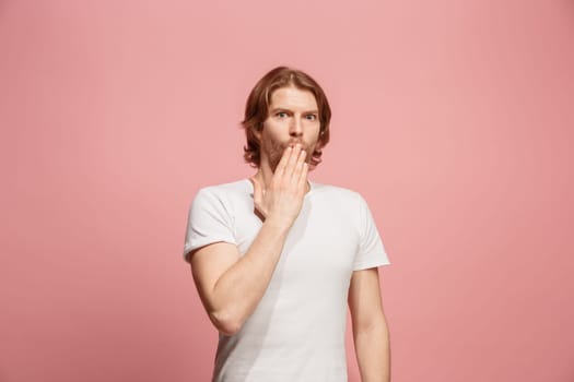 Secret, gossip concept. Young man whispering a secret behind her hand. Business man isolated on trendy pink studio background. Young emotional man. Human emotions, facial expression concept.