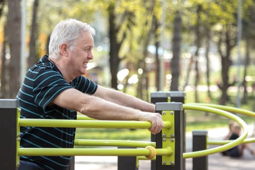 Old man resting after doing physical exercises in the fitness park