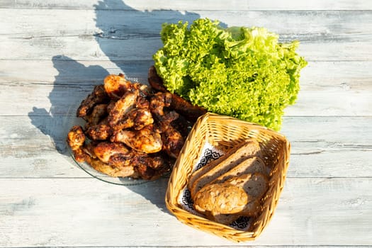 Close up on plate of fresh grilled meat surroundet by fresh salad and a whole grain bread in basked. Presented outdoor on wooden table.