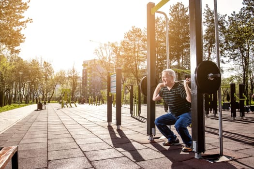 Elderly man making squats with weights in a fitness park (outdoors gym)