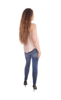 A pretty woman in a beige blouse, jeans and high heels with long.brunette hair standing from the back, isolated for white background.