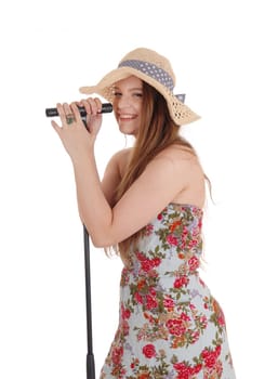 A beautiful woman in a colorful dress and hat standing and holding the.microphone and singing, isolated for white background..