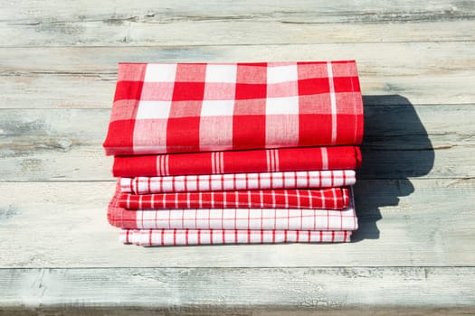 Stack of red white checkered and striped tableclothes on rustic bright wooden table. Outdoor.