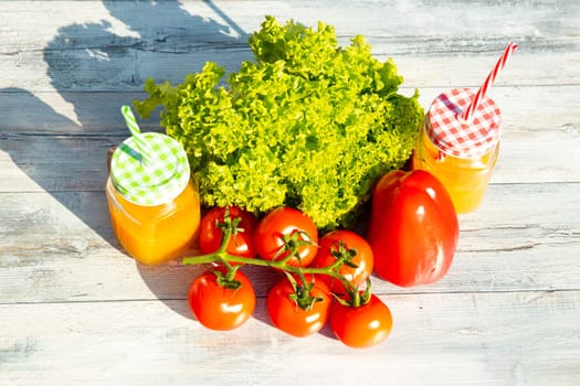 Healthy fresh salad, tomatoes, paprika and two glasses filled with fresh pressed orange juice. Presented outdoor on bright wooden table. Food health concept. .