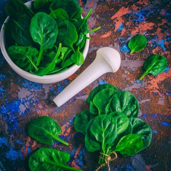 fresh green spinach leaves in a white ceramic mortar, near the pestle, top view