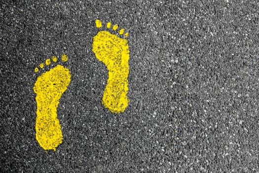 Yellow footprint signs on an asphalt road for pedestrian. Symbol of walkway.