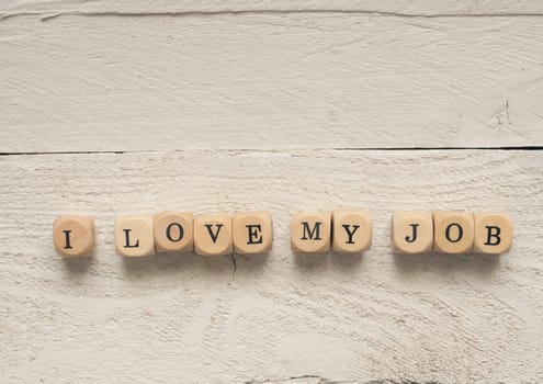 Wooden dices with the words I love my job on a white wooden table