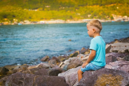 Cute caucasian boy sitting at seaside. Leisure time