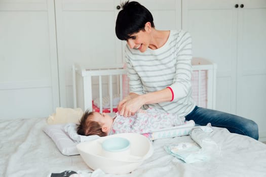 Baby has had her nappy changed by her mother on the double bed. The mother is fastening the baby grow while being playful.