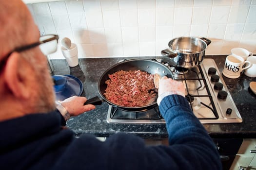 Over the shoulder shot of a mature man browning off mince to make a spagetti bolognese.