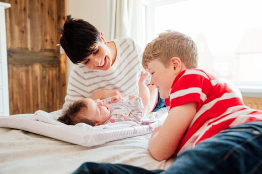 Little boy and his mother are being playful with the baby after changing her nappy on the bed.