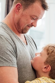 Little boy and his father are making eye contact while having a cuddle at home.