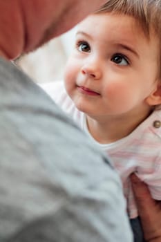 Baby girl is looking at her father while they have a cuddle at home.