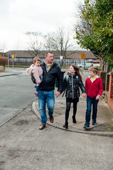 Mature man has just picked up his eldest daughter from school with his other two children. They are talking as they walk home together.